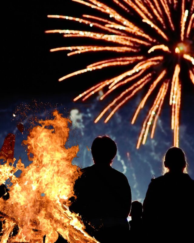 Silohette of family next to and infront of fireworks and bonfire